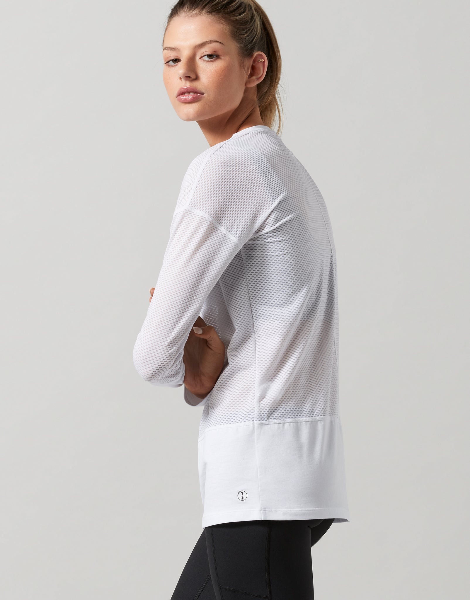 A model wearing a white long sleeved activewear top and black leggings.