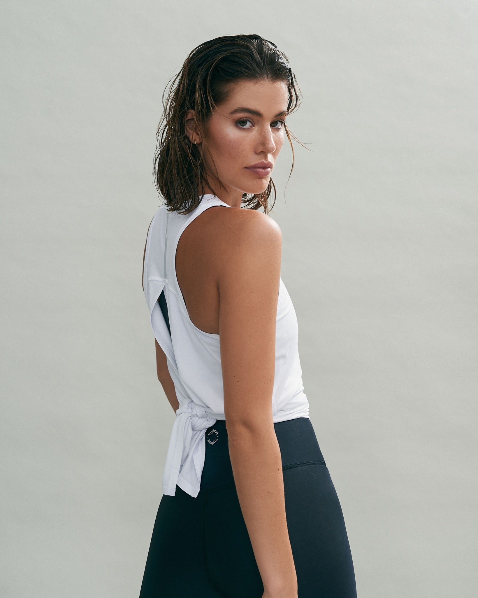 A woman wearing a white tie up activewear top and blue leggings.