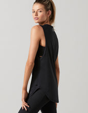 Woman wearing a black sleeveless top with cut-out design on a gray background