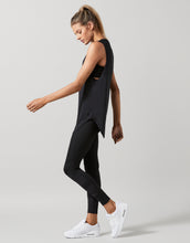 Woman wearing a black sleeveless top and leggings with white sneakers on a light gray background