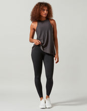 A woman wearing a grey tank top, white sneakers and black leggings on a white background