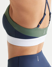 Close up of a sports bra top with green, navy, and white color block design on a white background