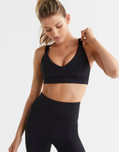 Woman wearing a black sports bra and leggings on a light gray background