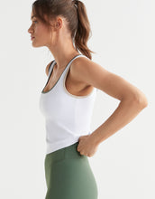 Woman wearing a white tank top and green leggings on a light gray background