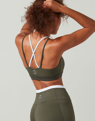A model in a sports bra in colors tarmac, white, and blue with contrast color block design, featuring a high-scooped neckline and strappy back.