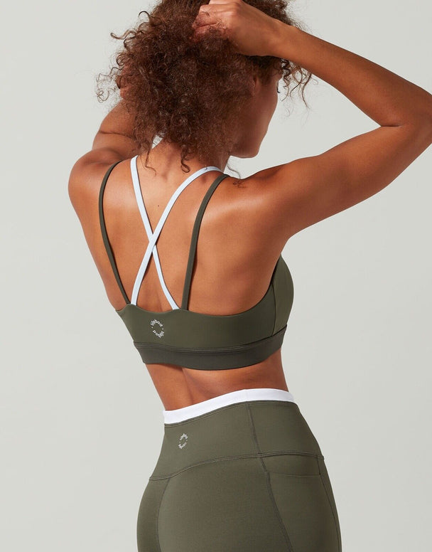 A model in a sports bra in colors tarmac, white, and blue with contrast color block design, featuring a high-scooped neckline and strappy back.
