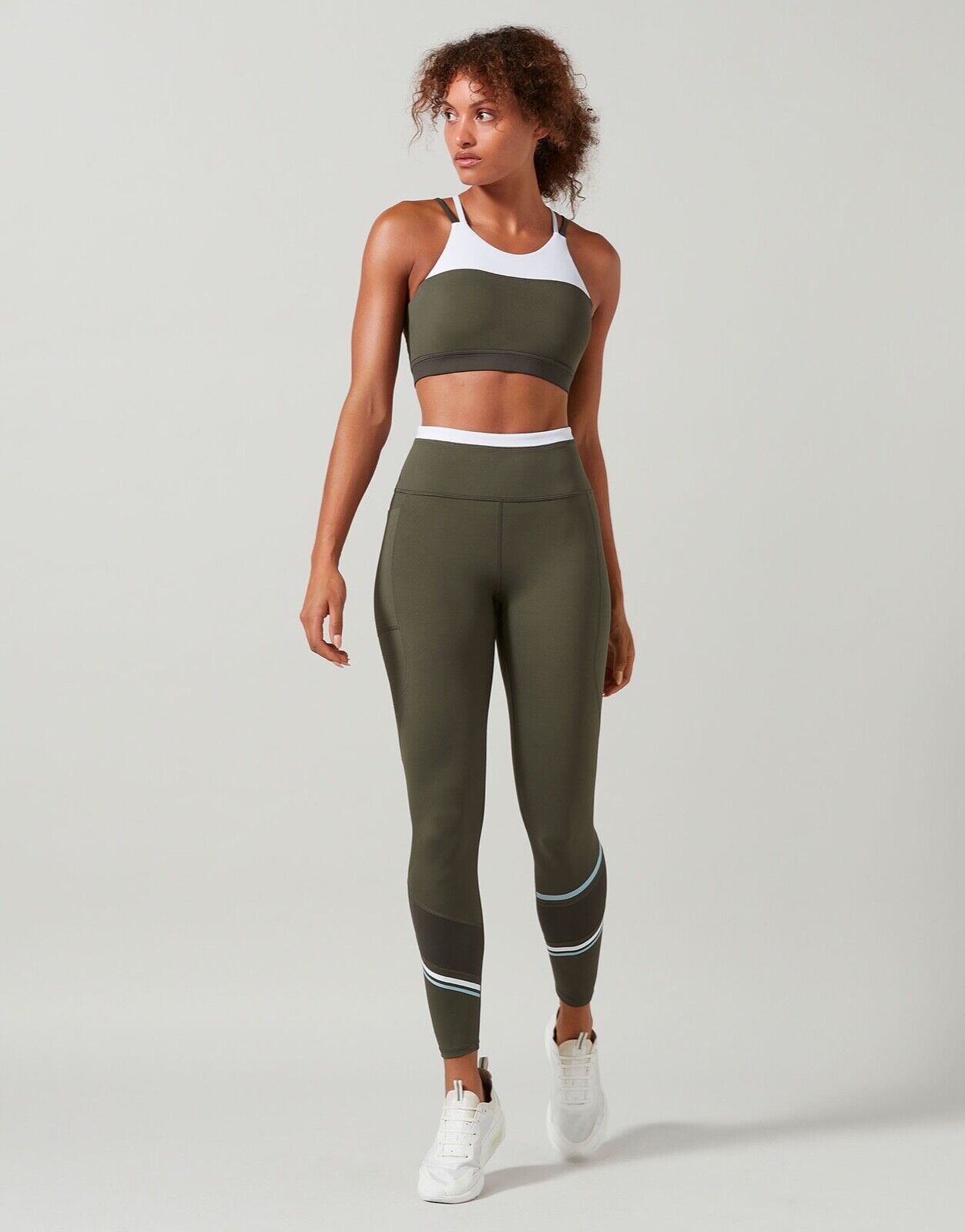 A model in a sports bra in colors tarmac, white, and blue with contrast color block design, featuring a high-scooped neckline and strappy back with matching leggings.