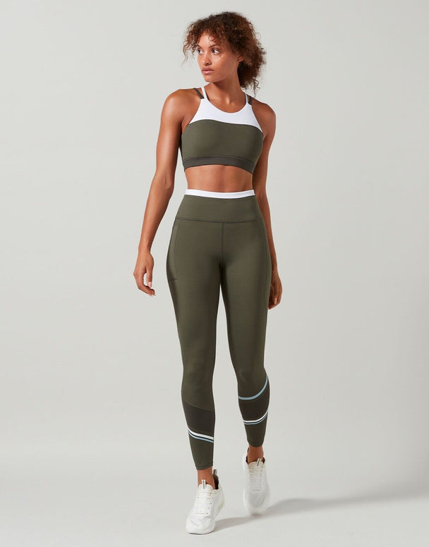 A model in a sports bra in colors tarmac, white, and blue with contrast color block design, featuring a high-scooped neckline and strappy back with matching leggings.
