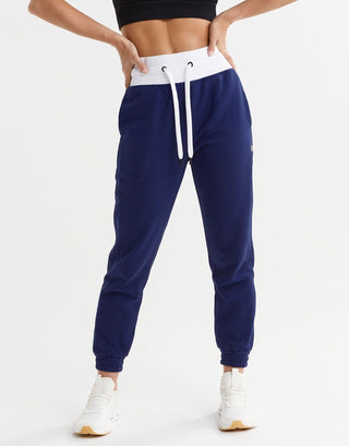 A person standing, facing to the side, wearing blue depth and bright white Lilybod Erica slim-fit sweatpants with a drawcord and elasticated leg cuff.