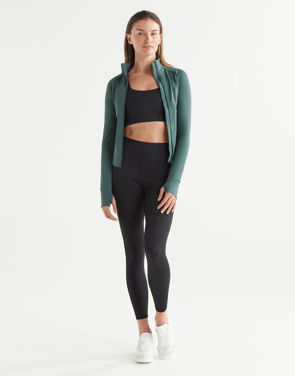 Woman wearing a green activewear jacket and black leggings on a white background