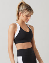 Woman wearing a black sports bra and leggings with white accents on a light gray background