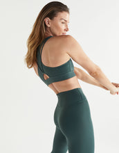 Woman wearing a green sports bra and leggings on a light gray background