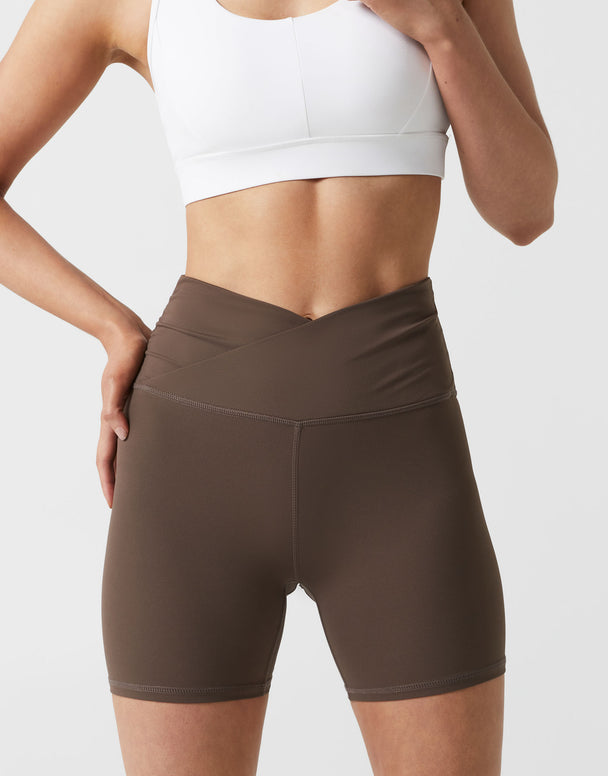 Person wearing brown athletic shorts and a white crop top on a light gray background