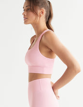 Woman wearing a pink sports bra and leggings on a white background