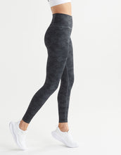 A woman wearing black stucco leggings and white runners on a white background