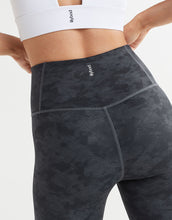 Person wearing black patterned leggings with a white sports bra on a light gray background