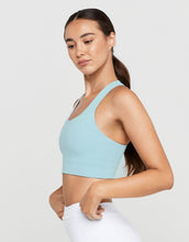 Woman wearing a light blue sports bra and white pants on a plain background