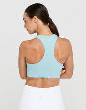 Woman wearing a light blue sports bra and white pants on a plain background