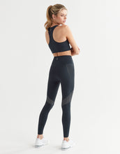Woman wearing a black sports bra and leggings on a white background