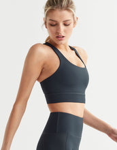 Woman wearing a dark blue sports bra and leggings on a light gray background