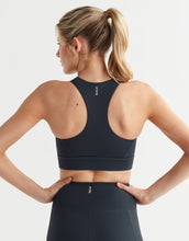 Woman wearing a navy sports bra and leggings on a light gray background