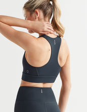 Woman wearing a black sports bra and leggings with a visible brand logo on a light gray background