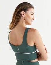 Woman wearing a green sports bra with a white band on a light gray background