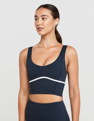 Woman wearing a navy sports bra with a white stripe on a light gray background
