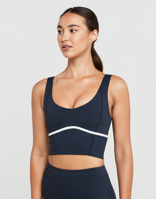 Woman wearing a navy sports bra with a white stripe on a light gray background