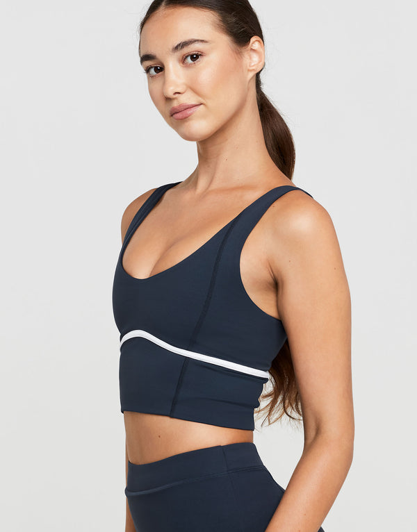 Woman wearing a navy sports bra with a white stripe on a light gray background