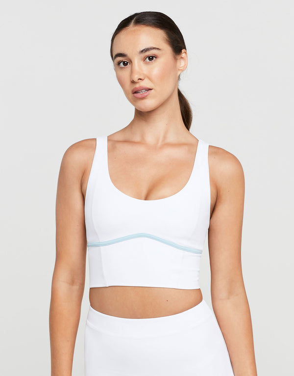 Woman wearing a white sports bra with a light blue stripe on a plain background