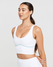 Woman wearing a white sports bra with a light blue accent on a plain background