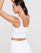 Woman wearing a white sports bra and leggings on a light gray background