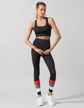 Woman wearing a black sports bra and leggings with colorful accents on a gray background