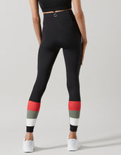 Black leggings with red, gray, and white striped cuffs worn by a person on a light gray background