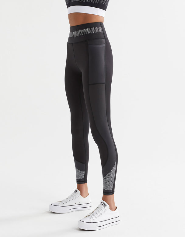 A person wearing black full length leggings with mesh printed paneling and double side pockets, paired with white sneakers.
