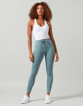 Woman wearing a white tank top and teal leggings on a gray background