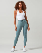 Woman wearing a white tank top and teal leggings on a gray background