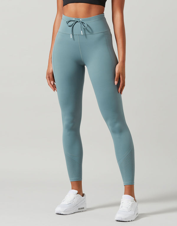 Woman wearing green activewear leggings on a plain background