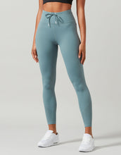 Woman wearing green activewear leggings on a plain background