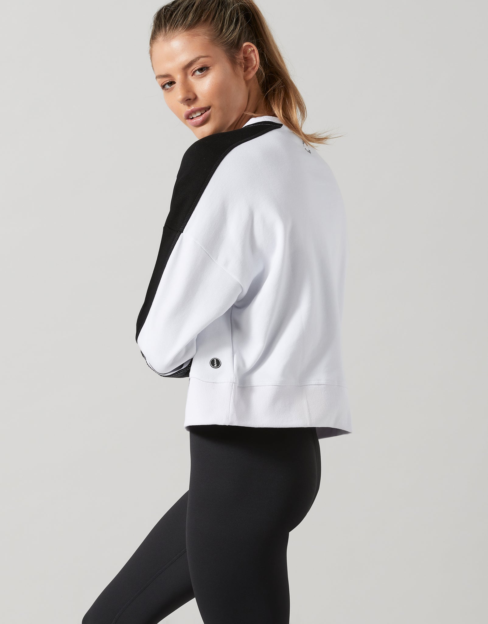 Woman wearing a white jacket over a black top and black leggings on a light gray background