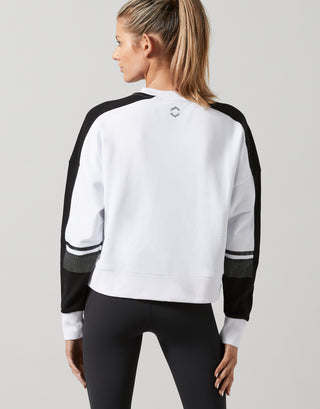 Person wearing a white and black sweatshirt with a logo on the back against a gray background