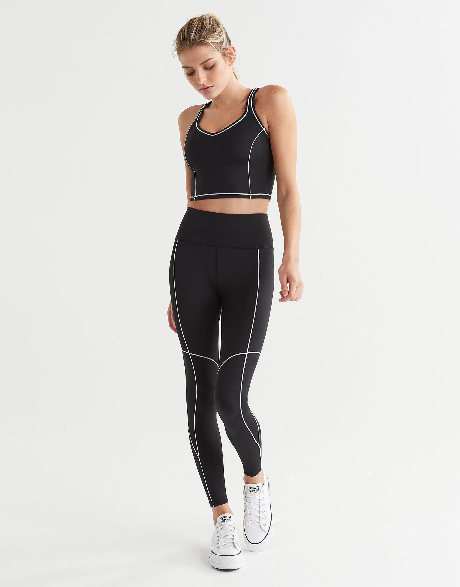 A woman wearing black leggings and a sports bra with white piping and white runners.
