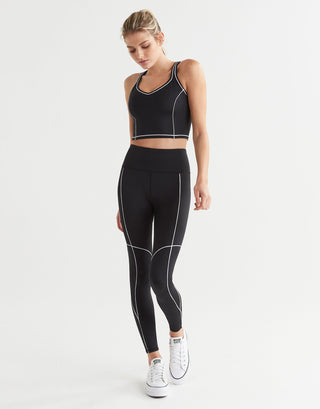 A woman wearing black leggings and a sports bra with white piping and white runners.