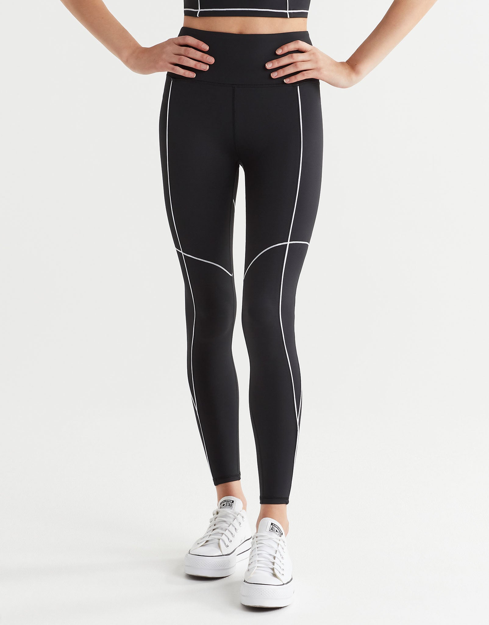A woman wearing black leggings with white piping ahd white runners.