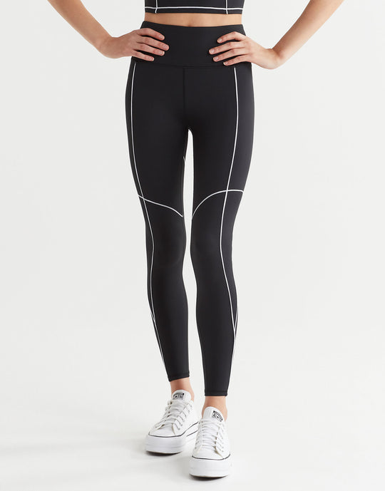 A woman wearing black leggings with white piping ahd white runners.