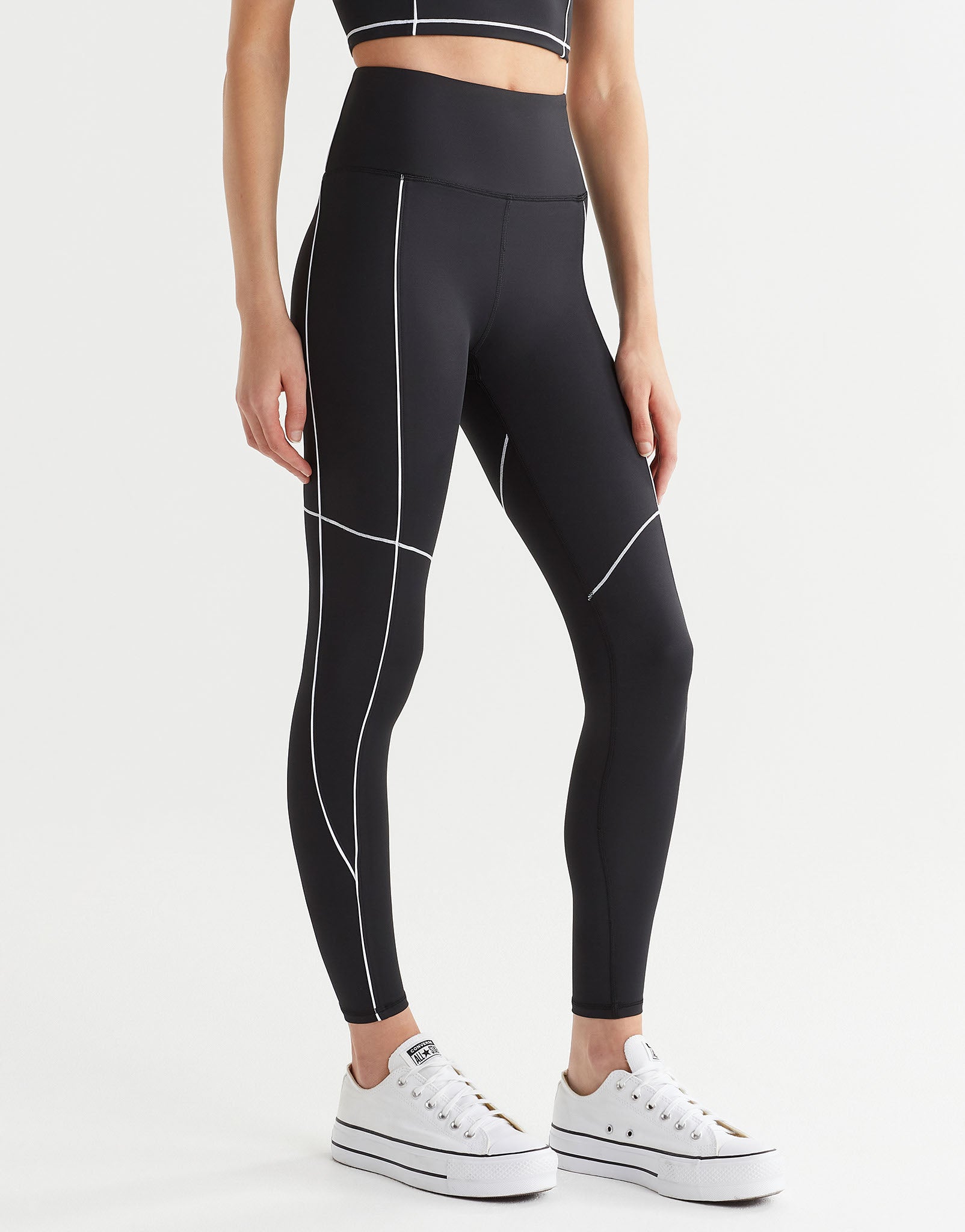 A model wearing black leggings with white piping and white runners.