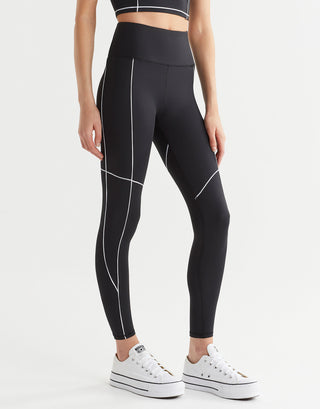 A model wearing black leggings with white piping and white runners.