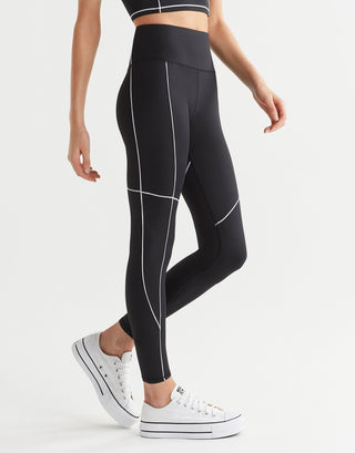 A woman wearing black leggings with white piping with white runners.
