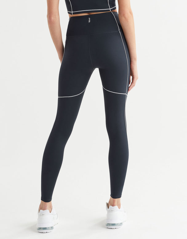 A person wearing full-length navy leggings with white contrast seaming and a V-point waistband.